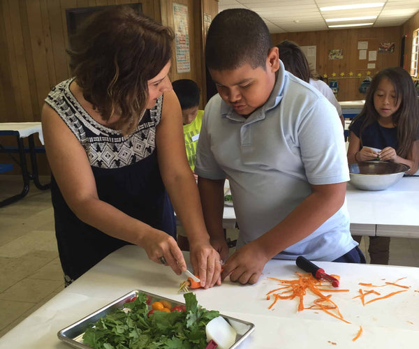 Woman helping a boy cut carrots to prepare a salad